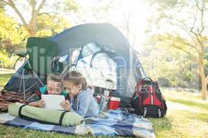 Siblings using laptop outside the tent at campsite