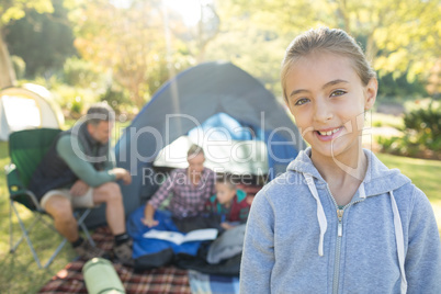 Girl smiling at camera while family sitting at tent in background