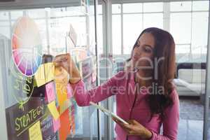 Female designer holding adhesive notes on glass in office