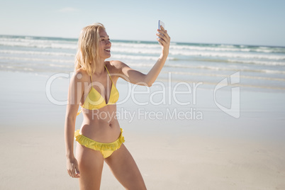 Happy young woman in yellow bikini taking selfie at beach