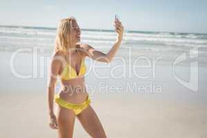 Happy young woman in yellow bikini taking selfie at beach