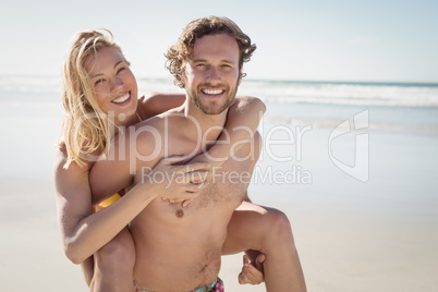 Portrait of young man piggybacking beautiful woman at beach