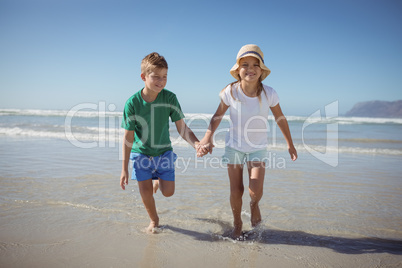 Happy siblings holding hands while running at beach