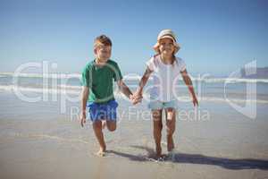 Happy siblings holding hands while running at beach