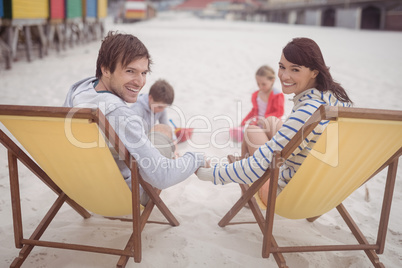 Portrait of parents relaxing on launge chairs with children playing in background