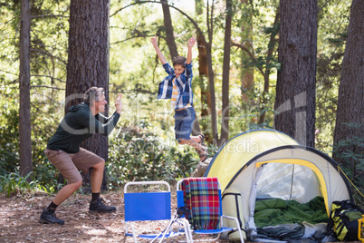 Father photographing playful boy jumping at campsite