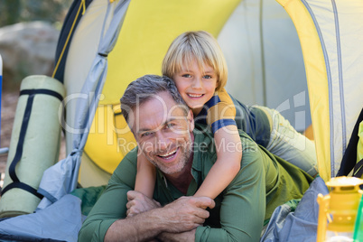 Little boy lying on father in tent at campsite