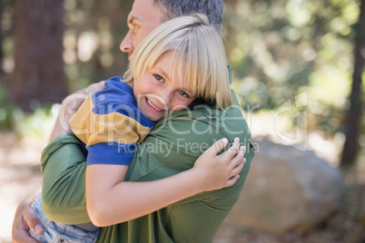 Smiling boy embracing father in forest