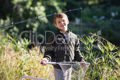 Portrait of smiling boy holding fishing net while standing in forest