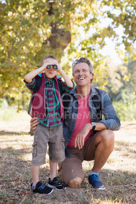 Happy father kneeling by boy looking through binoculars