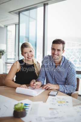 Portrait of smiling executives discussing over paper at desk