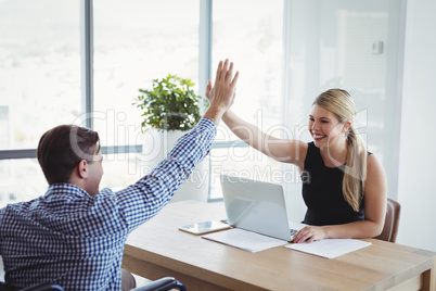 Smiling executives giving high-five to each other at desk