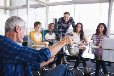 Businessman showing mobile phone to team working in background