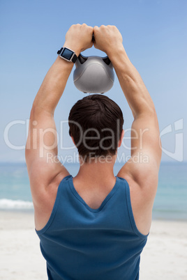 Rear view of young man lifting kettlebell at beach