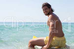 Smiling surfer sitting on surfboard at seacoast