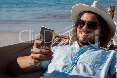 Man relaxing on hammock and using mobile phone on the beach