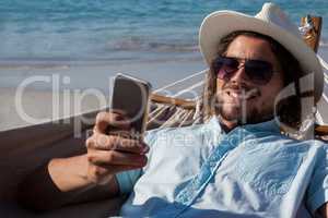 Man relaxing on hammock and using mobile phone on the beach