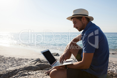 Man sitting on the rocks and using laptop on beach