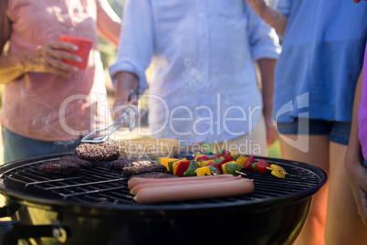 Family grilling patties, vegetables and sausages on the barbecue grill