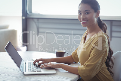 Smiling businesswoman using laptop on desk in office