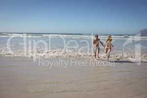 Full length of couple running on shore at beach