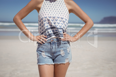Mid section of woman with hands on hip standing at beach
