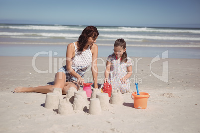 Happy girl with mother making sand castle at beach