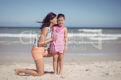 Happy mother kissing her daughter at beach