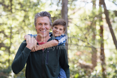 Happy father piggybacking son while hiking in forest