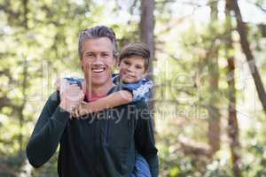 Happy father piggybacking son while hiking in forest