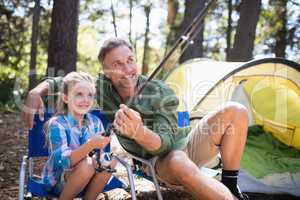 Father and daughter fishing at campsite in forest