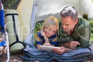Father and son using digital tablet while resting at campsite