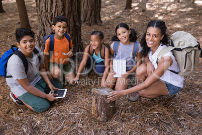 High angle portrait of teacher and students kneeling by tree stump