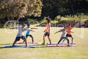 Female trainer watching children praciticing Virabhadrasana II pose