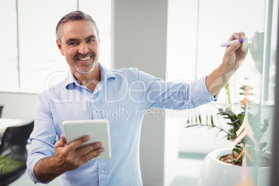 Portrait of smiling executive using digital tablet while writing on whiteboard