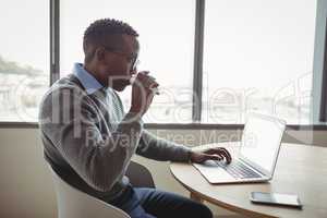 Attentive executive drinking coffee while using laptop