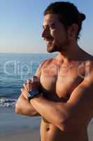 Muscular man standing with arms crossed at beach
