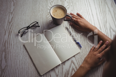 Hands of businesswoman by notebook and coffee cup on table