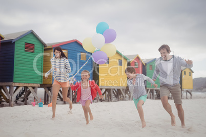Happy family holding balloons while running at beach