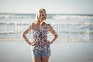 Portrait of smiling woman standing with hands on hip at beach