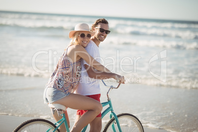 Smiling couple riding bicycle at beach