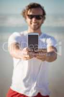 Smiling man holding mobile phone at beach