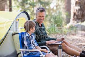 Father talking to son while using laptop in forest