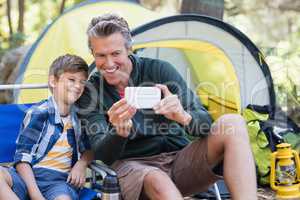 Father and son taking selfie by tent in forest