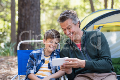Happy father showing mobile to son in forest