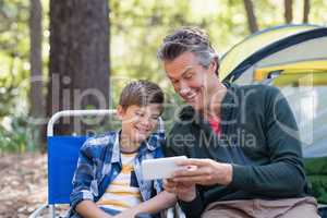Happy father showing mobile to son in forest