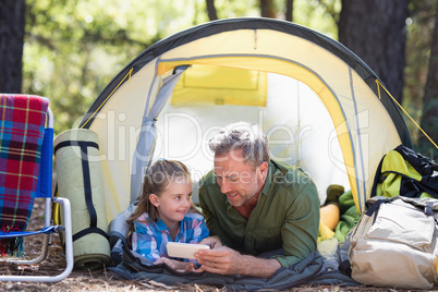 Father and daughter using mobile phone while relaxing in tent