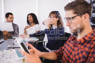 Businesswoman drinking water while sitting with colleagues