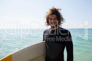 Smiling surfer with surfboard standing at beach coast