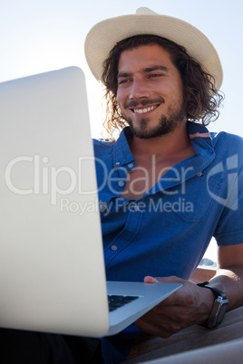 Happy man using laptop while relaxing on hammock at beach